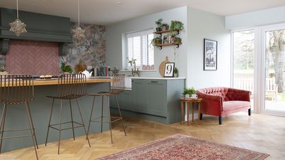 Open plan shaker kitchen with green units, brass bar stools and pink sofa
