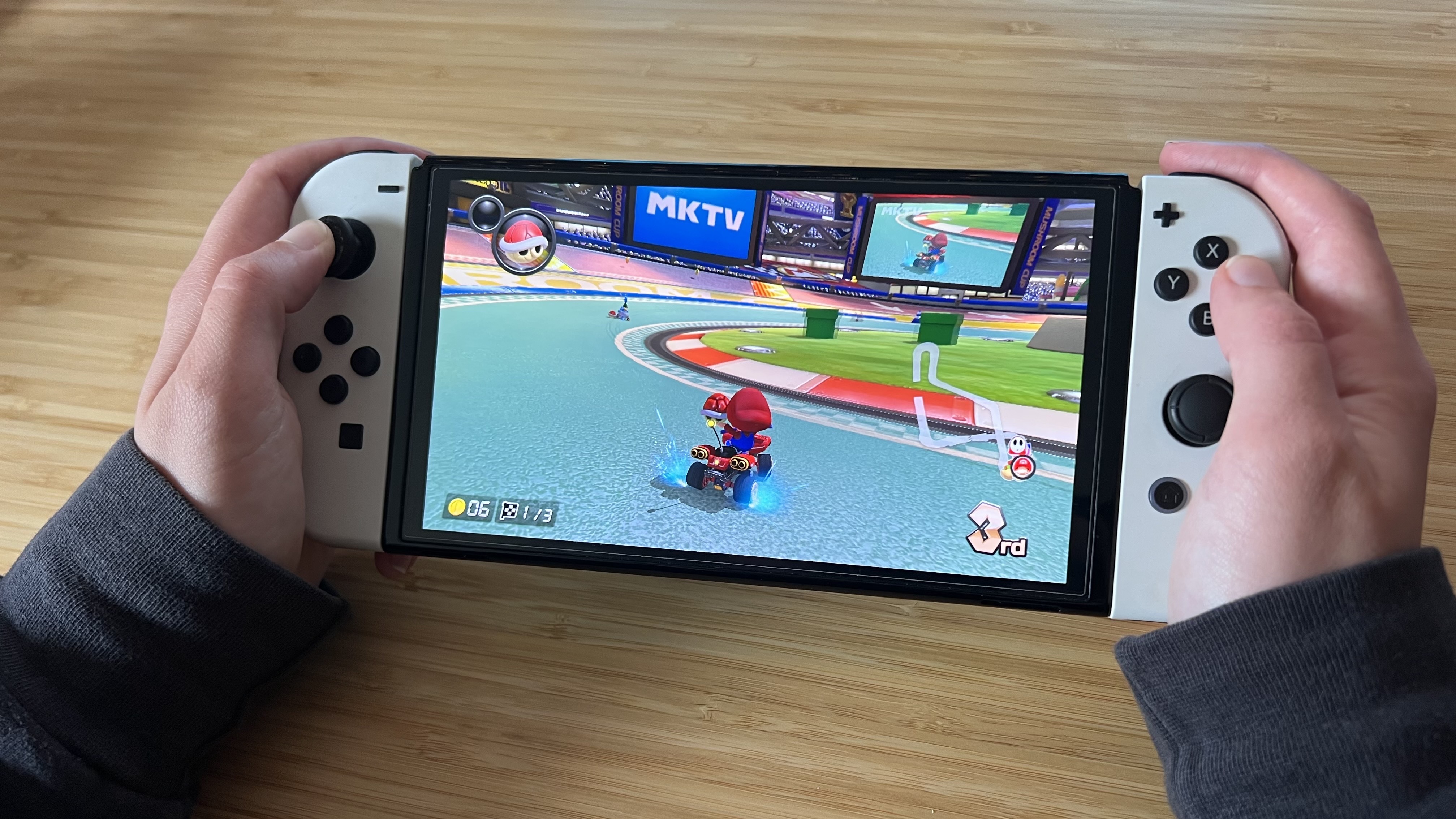 Hands holding Nintendo Switch OLED and playing Mario Kart 8 Deluxe