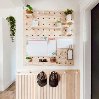 A pegboard in a hallway with a calendar and plants on it