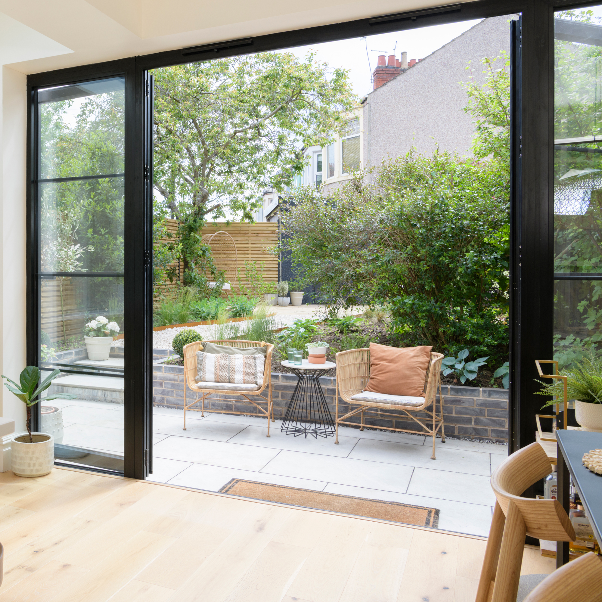 patio doors from a kitchen leading out into a large landscaped garden with a bistro set for two