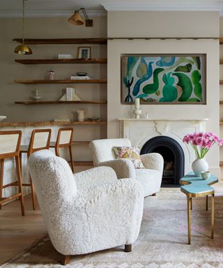 A living room with white boucle armchairs, open shelving, and a large piece of art over a mantle