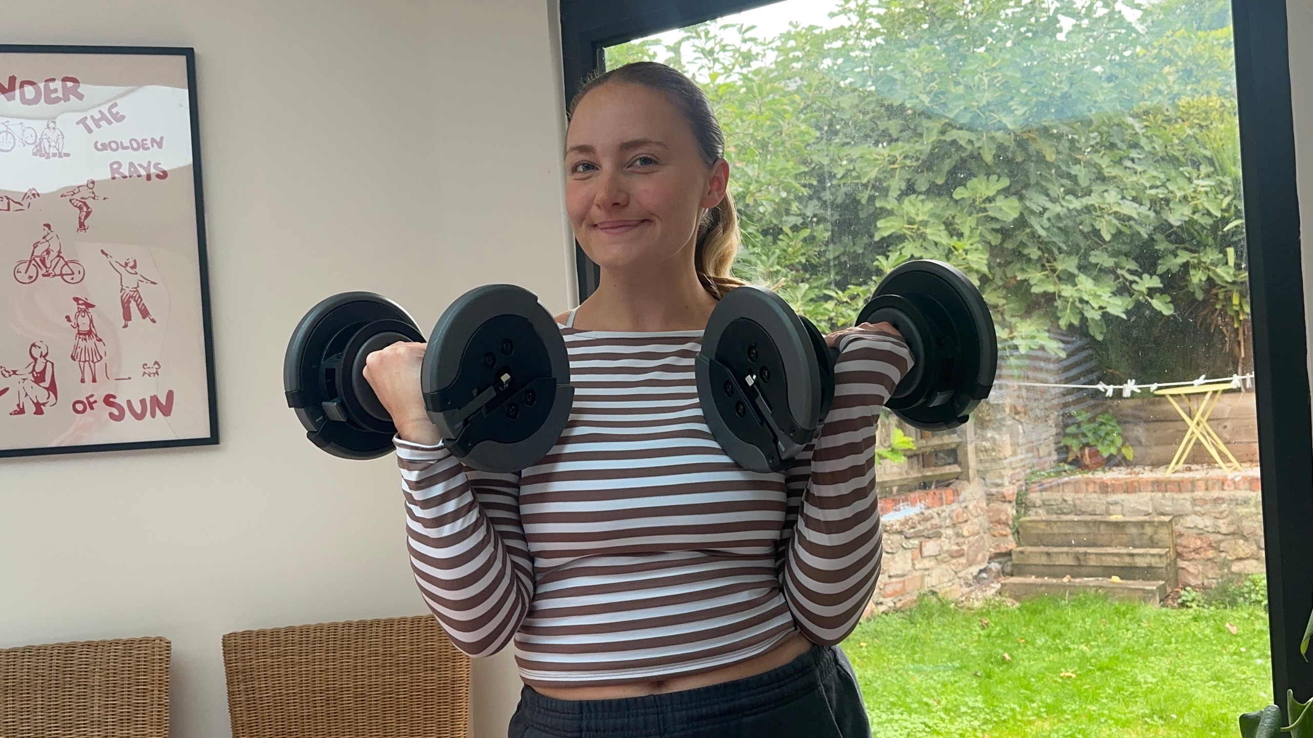 Alice Porter holds NordicTrack Select-a-weight dumbbells up at her shoulders in her living room.