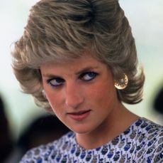 Princess Diana wearing a white printed dress and gold earrings looking skeptical