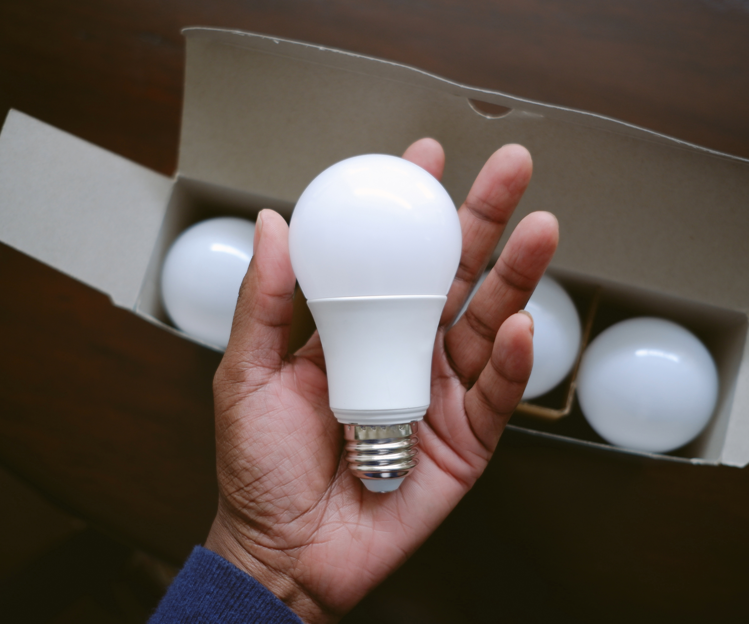 LED bulb in someone&#039;s hand with a box of other bulbs below