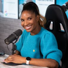 Denise Lewis in a studio wearing a blue jumper, presenting her podcast