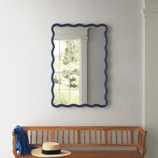A blue wavy mirror hanging above an entryway bench