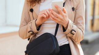 woman wearing crossbody handbag typing on phone