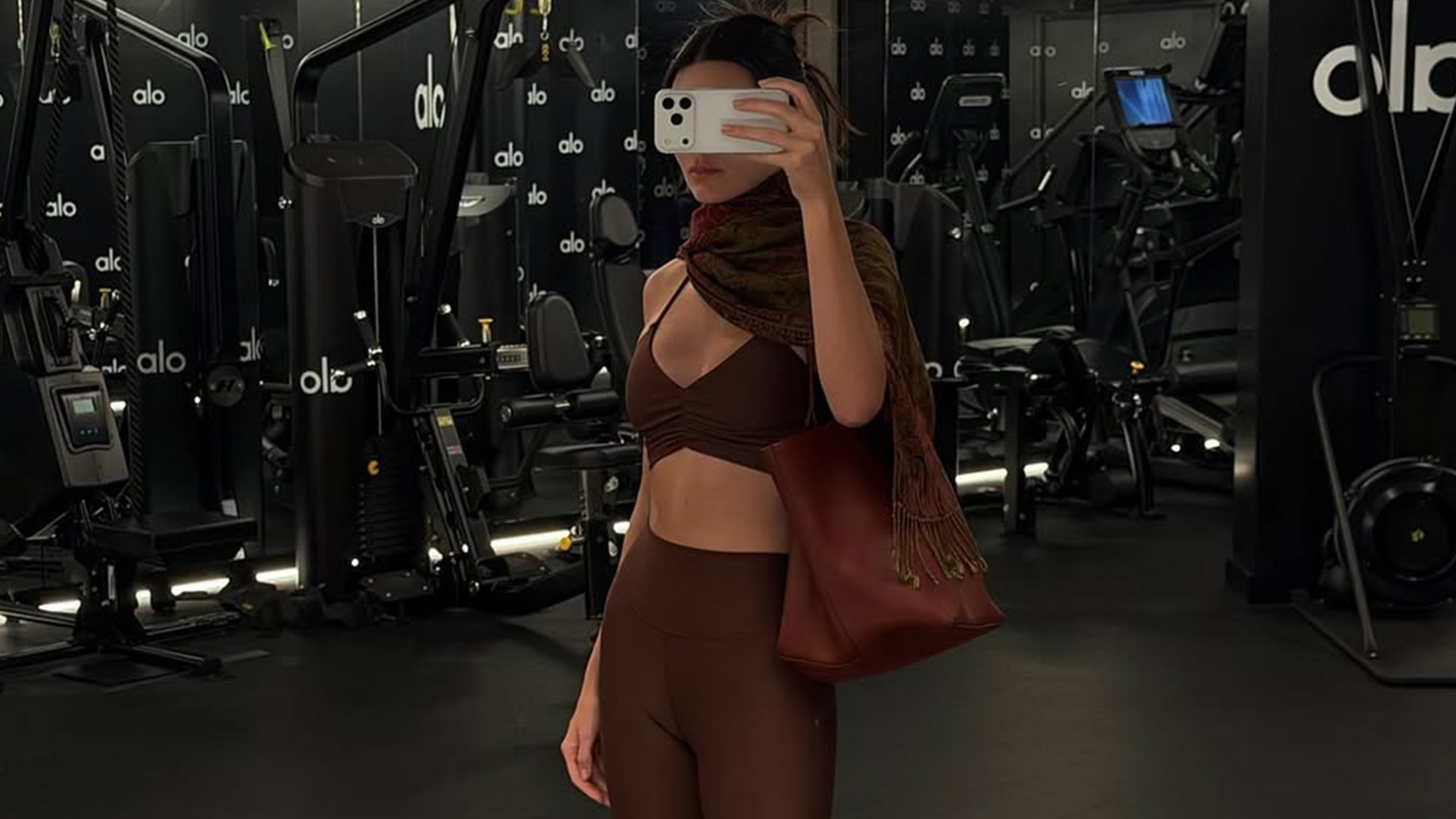 Kendall wears a brown scarf, tan leather bag, brown sports bra, brown leggings.