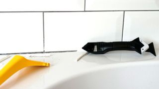 Silicone/caulk removal tool on a bath against a background of white metro tiles