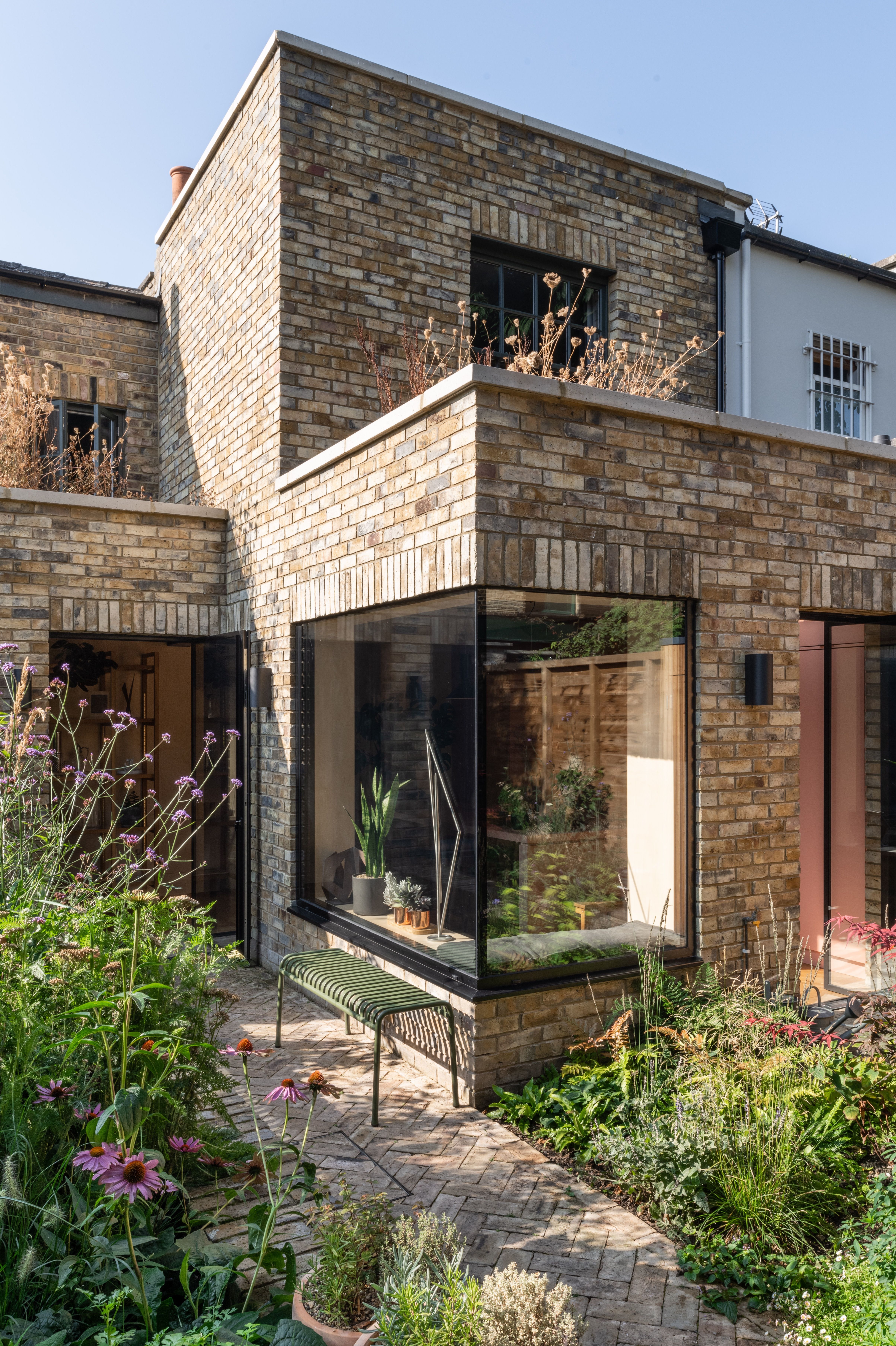 Urban garden with herringbone brick terrace, lush planting and green HAY Palissade bench