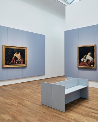 Light blue solid wooden bench seats in art gallery showing Two paintings on adjacent walls