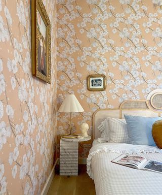 pink floral wallpapered bedroom with a large bed styled with gingham bedding and a marble side table with a brass table lamp and scalloped shade