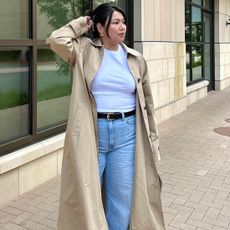 female fashion influencer Marina Torres poses with a butterfly clip up-do hairstyle, statement earrings, basic white t-shirt, trench coat, black belt, and jeans