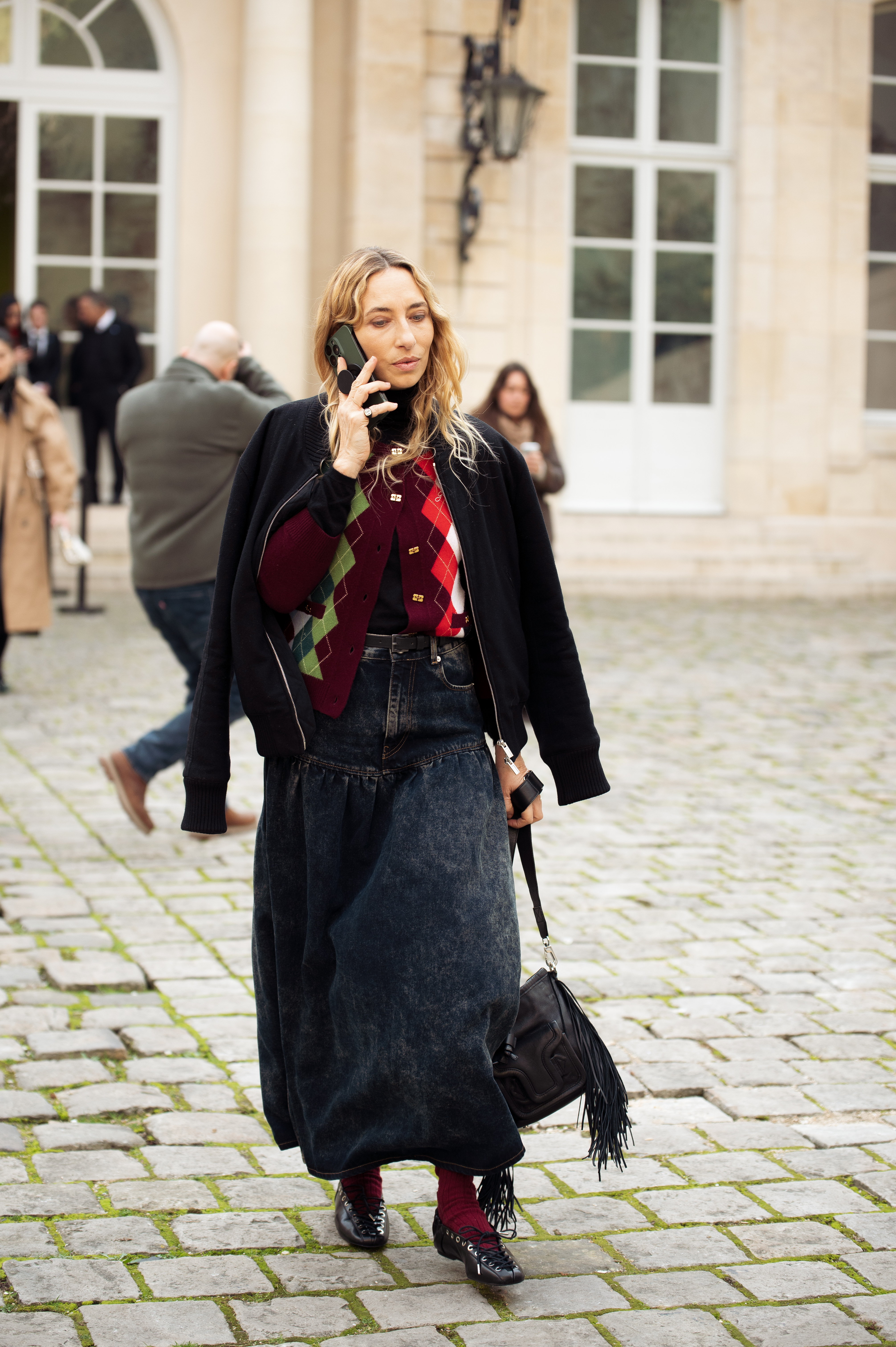 PARIS, FRANCE - MARCH 04: A guest wears dark blue denim skirt, black jacket, black bag, burgundy socks, black pointy shoes, burgundy, red and green sweater outside the Ganni fashion show during the Womenswear Fall/Winter 2025/2026 as part of Paris Fashion Week on March 04, 2025 in Paris, France. (Photo by Raimonda Kulikauskiene/Getty Images)