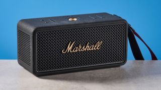 The Marshall Middleton II Bluetooth speaker in Black and Brass, on a stone surface with a blue wall in the background