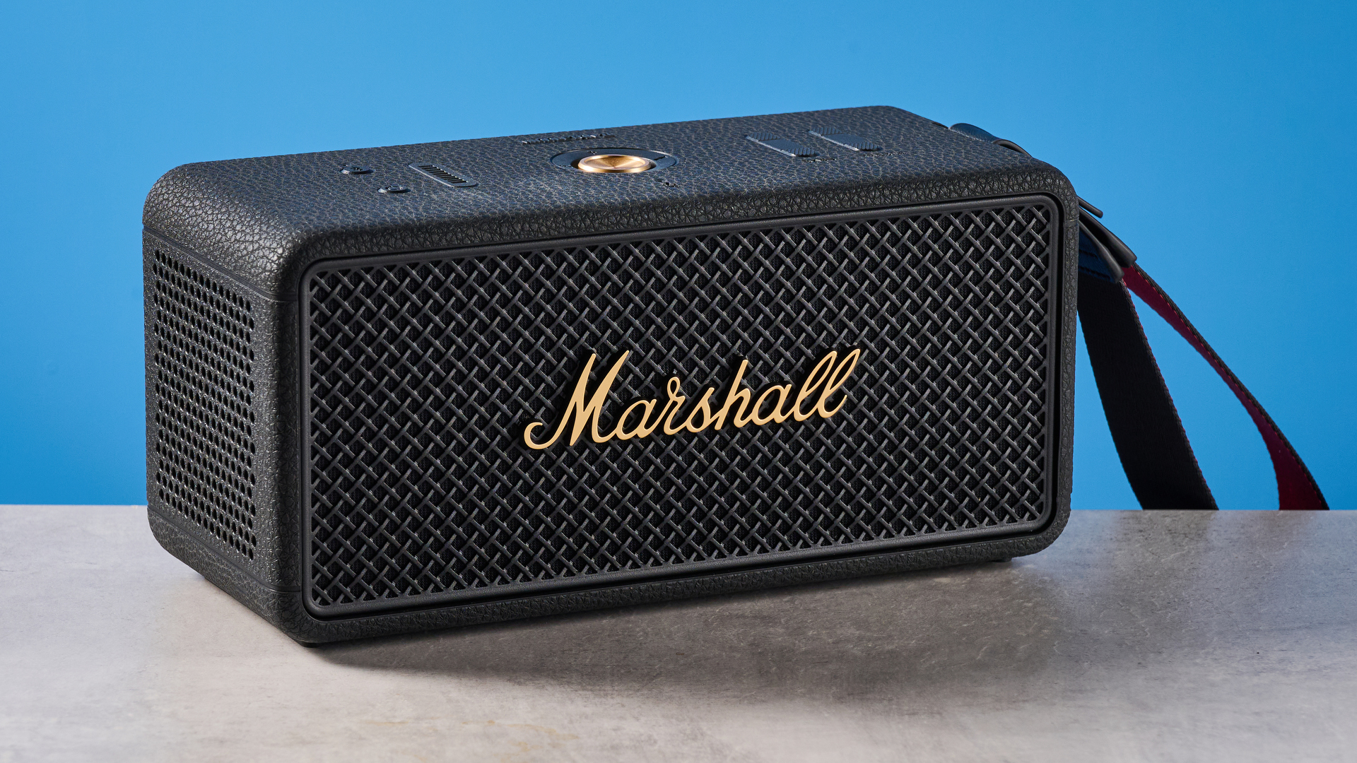 The Marshall Middleton II Bluetooth speaker in Black and Brass, on a stone surface with a blue wall in the background