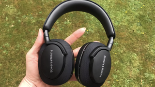 De trådløse hotetelefonene Bowers & Wilkins PX7 S2 i en hånd over en gressplen.