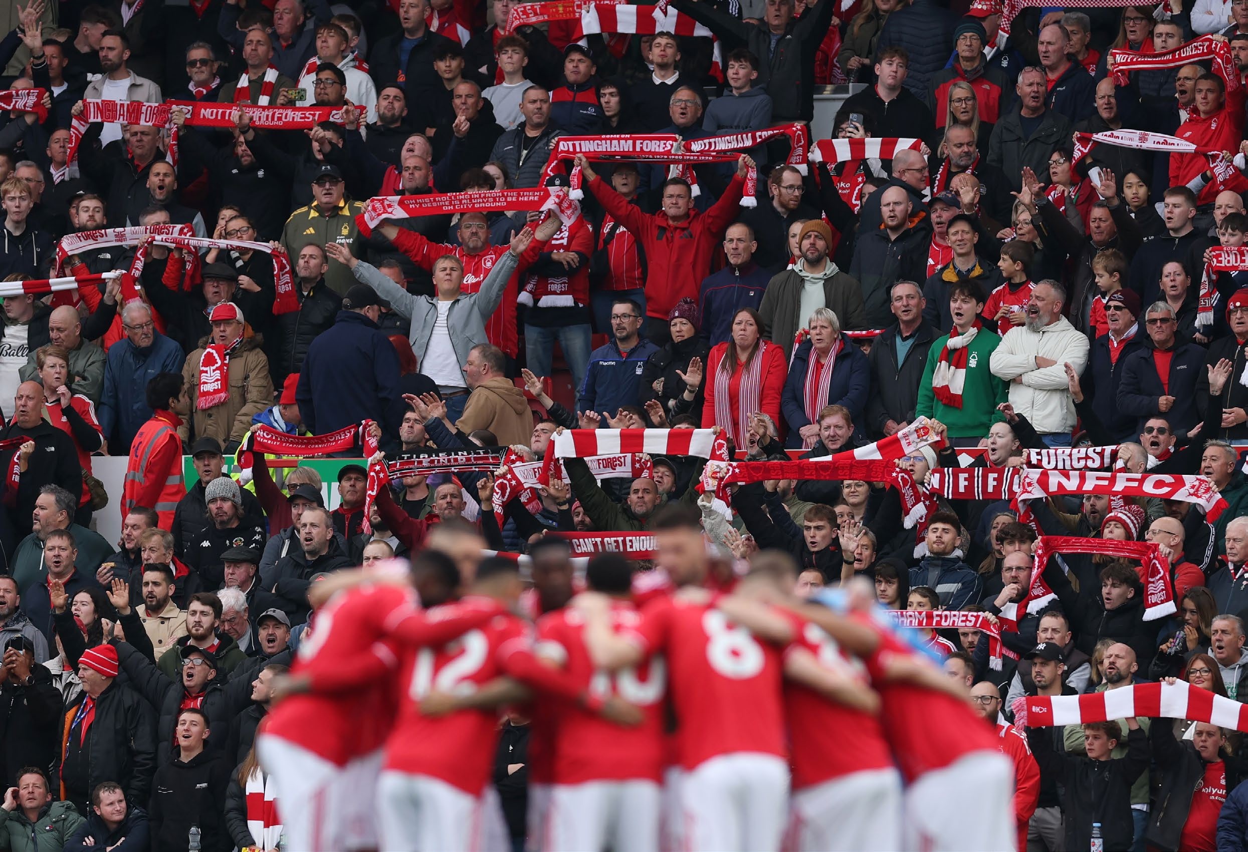 Forest players in a huddle, fans watching on.
