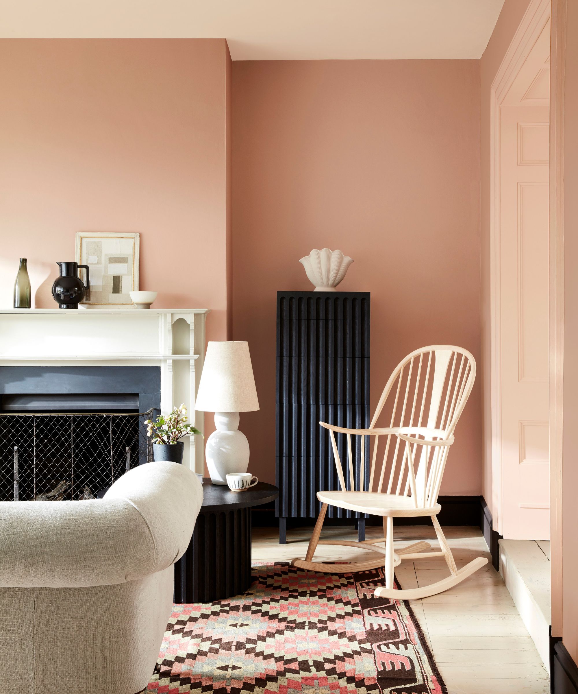 sitting room with plaster pink walls, patterned pink rug, fireplace and rocking chair