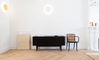 Black sideboard and black and cane chair against a white wall on a wooden floor