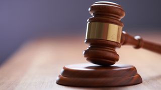 Close up picture of a gavel hammer placed on wooden table top.