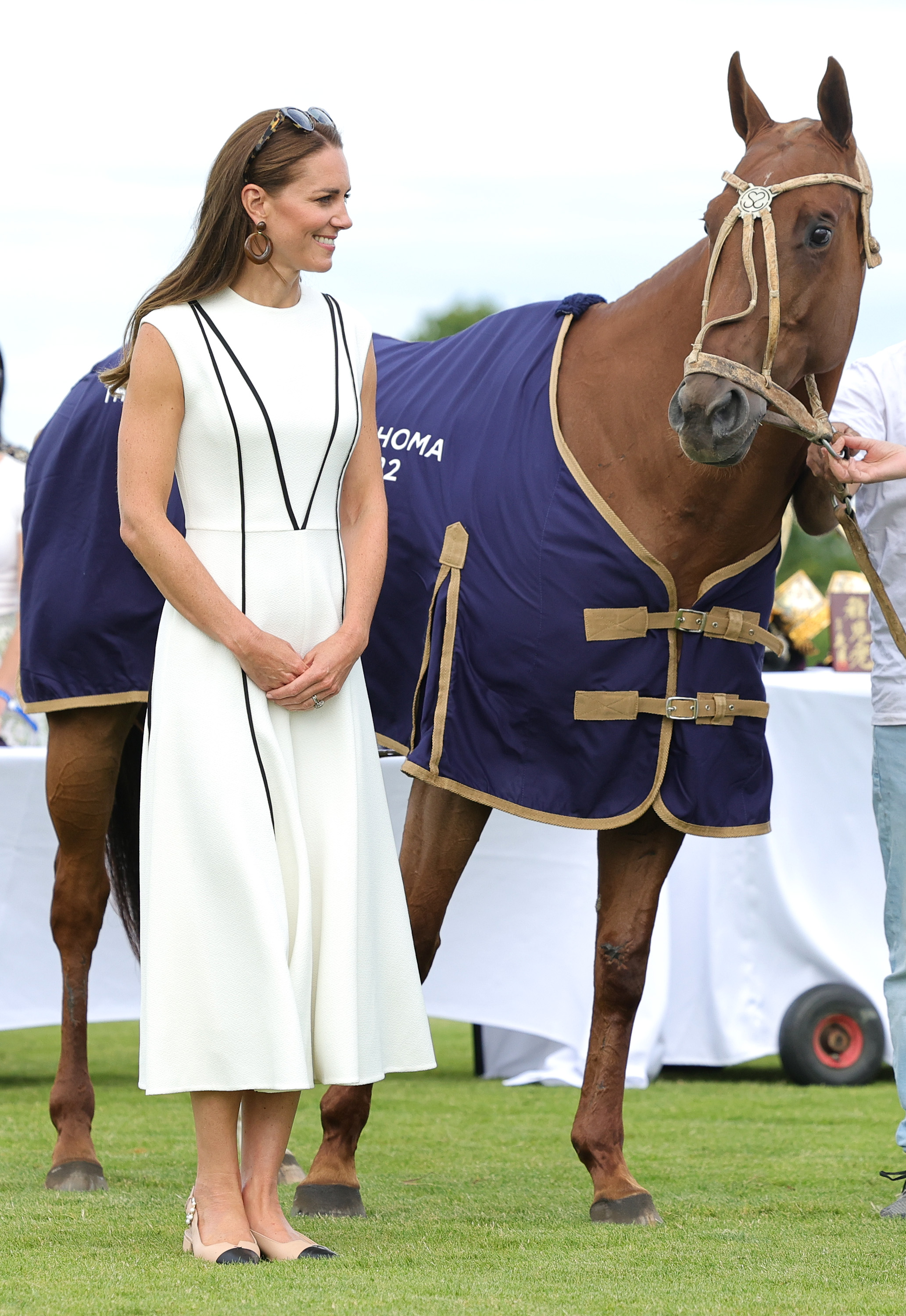 Princess Kate wearing a sleeveless ivory dress standing next to a horse