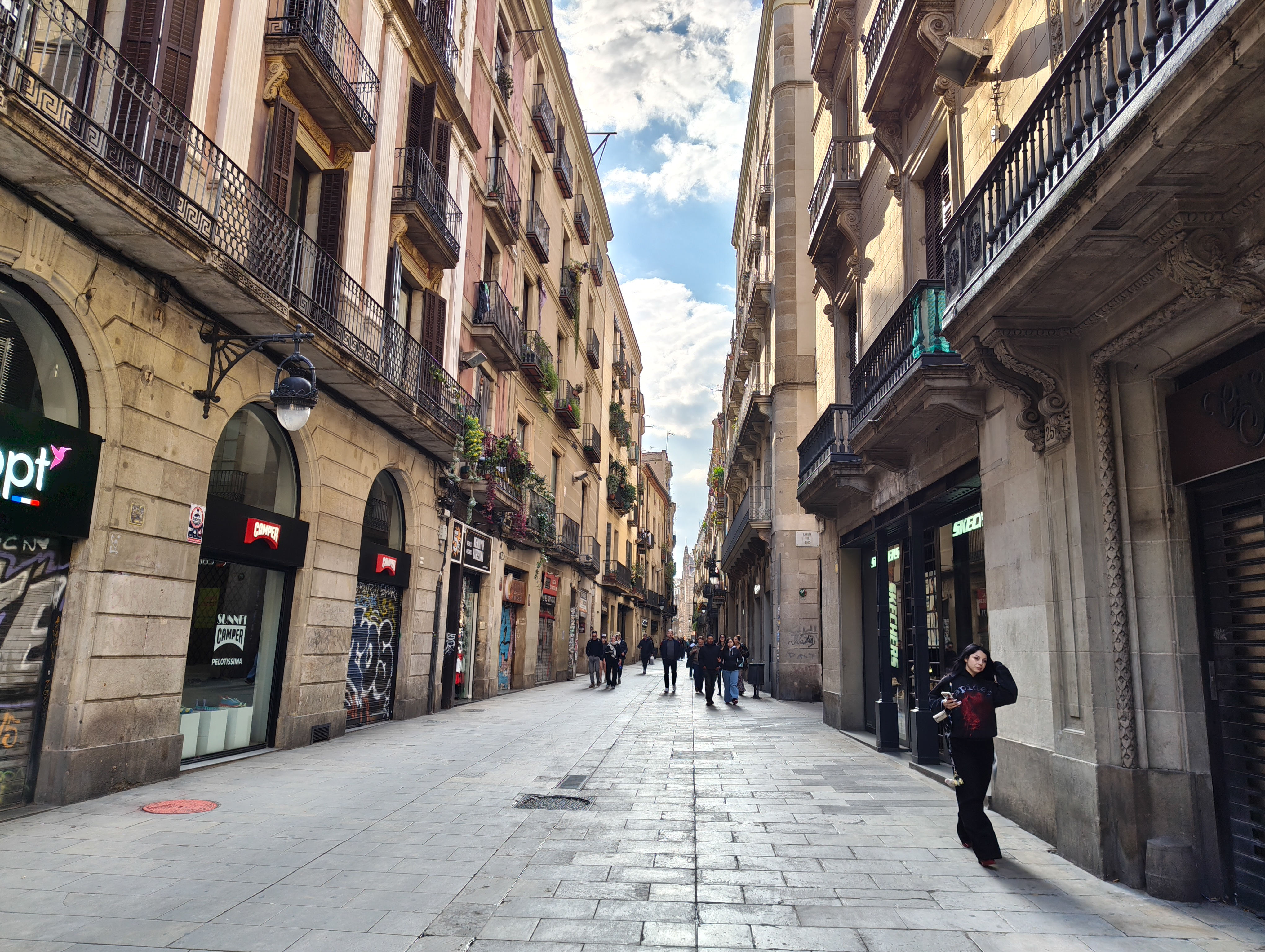 Pedestrians walking along a narrow Barcelona street lined with shops and historic buildings, photographed with the Nothing Phone (4a).