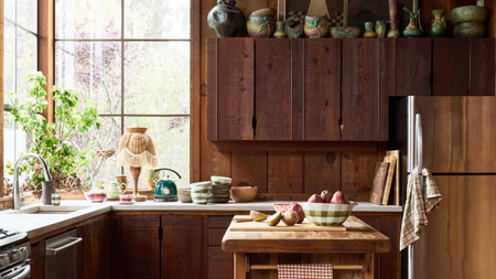 a cozy kitchen with rustic wood cabinets, large windows in the corner, and a bowl of fruit on the butcher block island