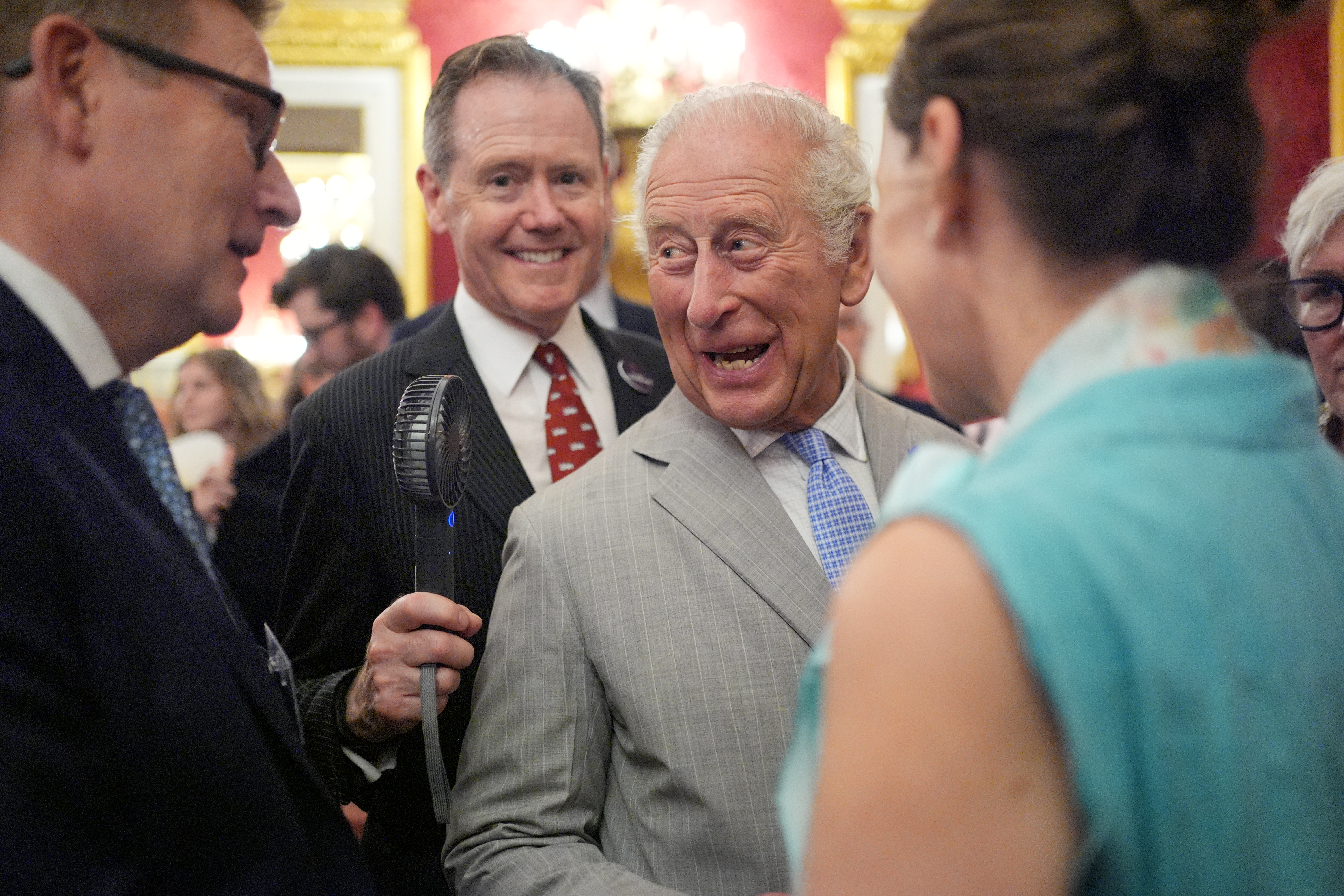 An aide holding a fan up to King Charles