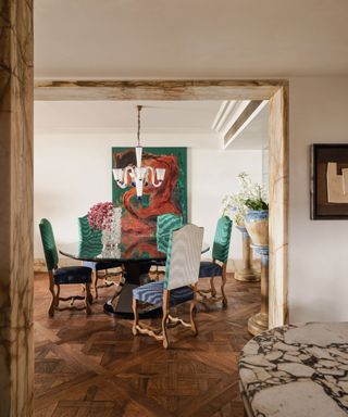 Dining room with wooden patterned floorboards and colorful upholstered chairs and colorful abstract artwork