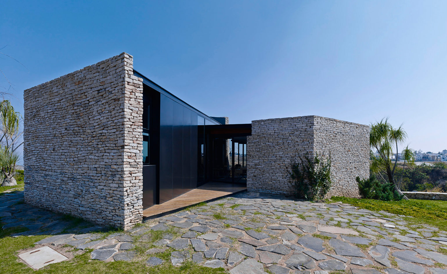 Exterior view of the Pabellón Río Blanco Mexico featuring stone walls and black glass details. Cracked slab detail driveway with trees in the surrounding