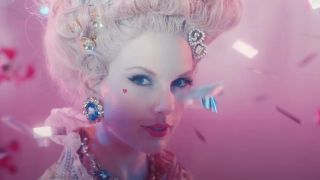 Taylor Swift in a powdered wig with hair clips that are S and N in the Bejeweled music video.