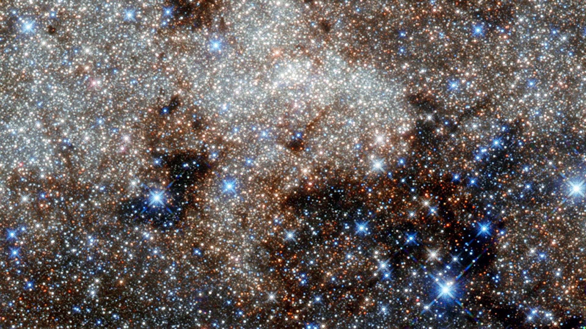 A view of white glowing gas swirling among white and blue stars in deep space.