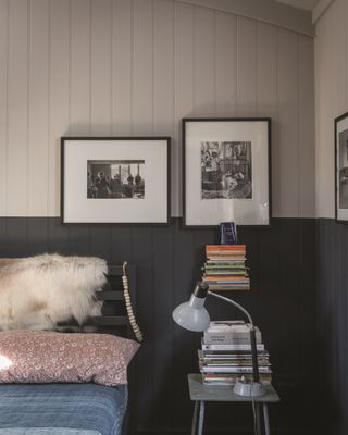 A bedroom with shiplap wall paneling painted in Farrow and Ball Railing and Estate Eggshell, with a bedside table with books on and framed art