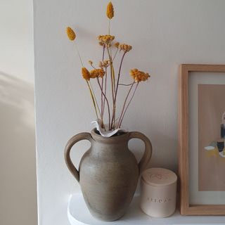 A vase with a flower frog made from air dry clay with dried flower stems placed on a mantelpiece