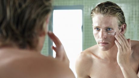 Man applying moisturiser while looking in the bathroom mirror