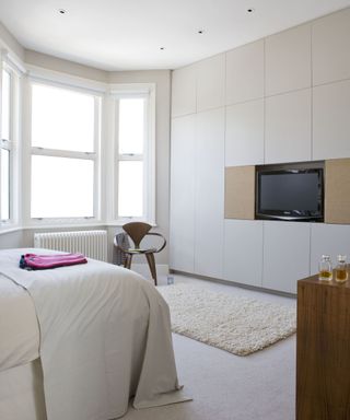 A bedroom TV idea with white bed and wall decor, with TV installed as part of white wardrobe unit