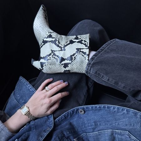 Snake skin print boots with black jeans and denim shirt and hand wearing gold watch and rings 