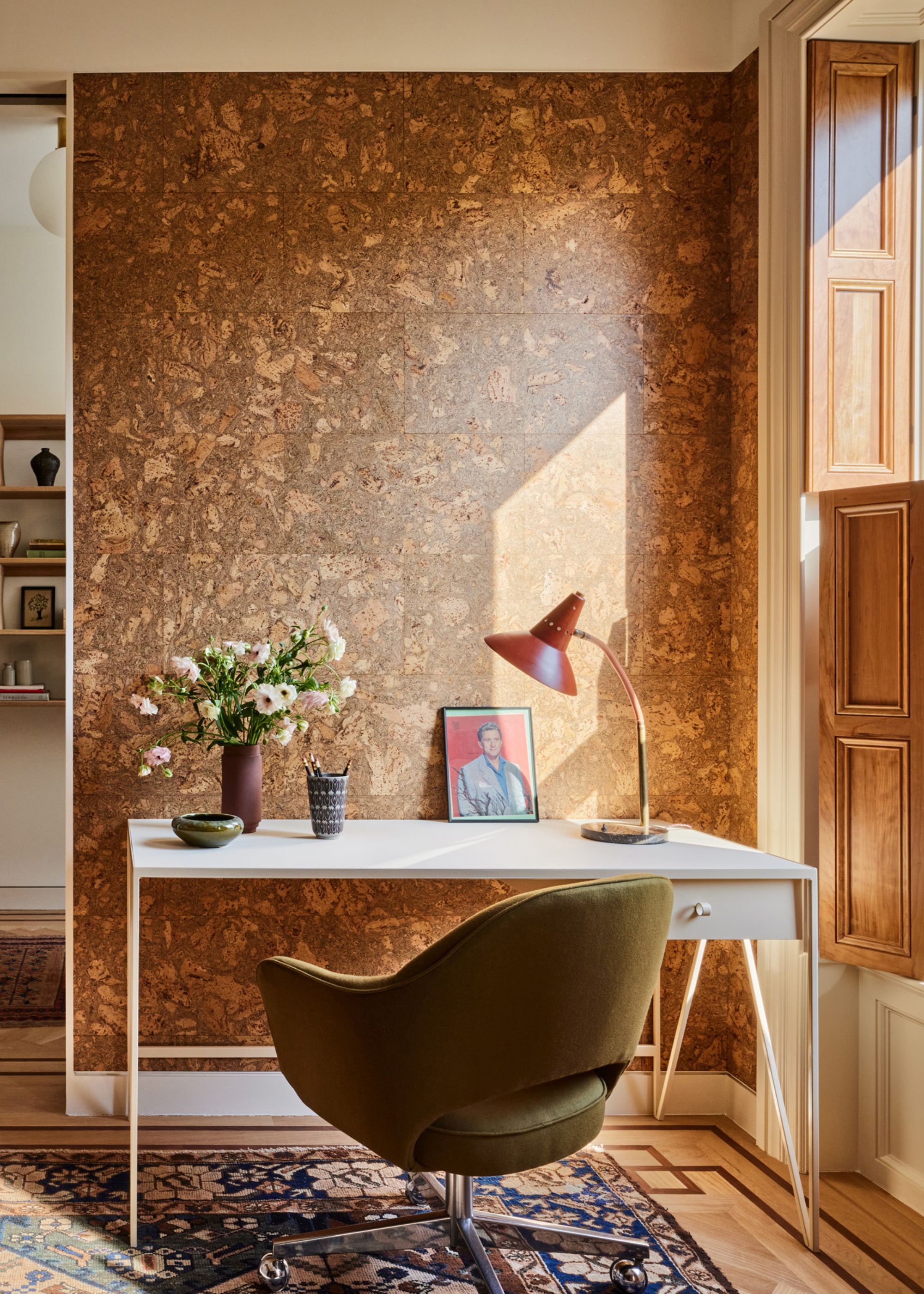 A study with a cork wall, a white desk, a green swivel chair, and a rug