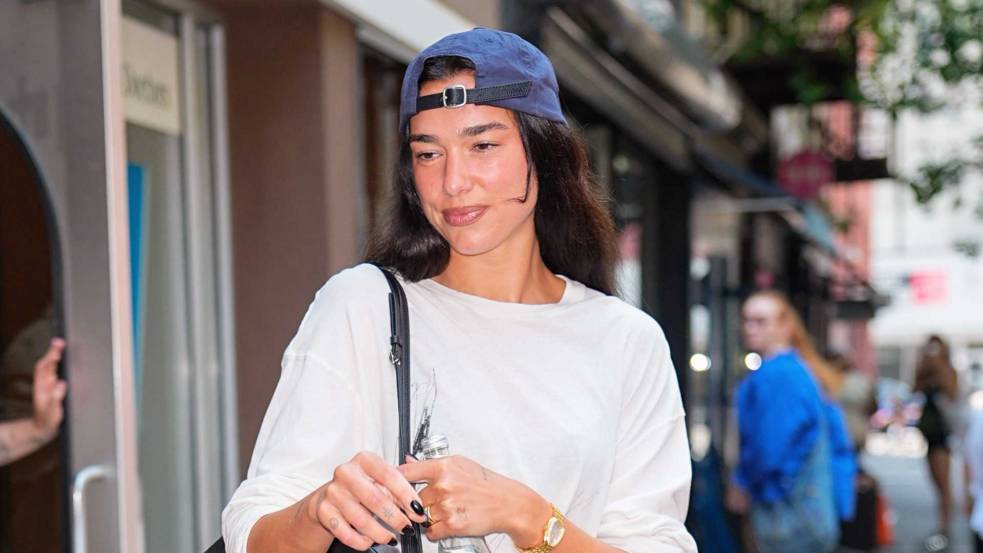 Dua Lipa exiting Electric Lady in NYC wearing a backwards baseball cap, white long-sleeve T-shirt, cut-off denim shorts, and a black Chanel Maxi Flap bag and burgundy Chanel Coco Beach ballet flats 