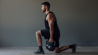 Male performing a kettlebell lunge holding a kettlebell in each hand in studio