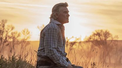 Kurt Russell sitting in a sunlit field