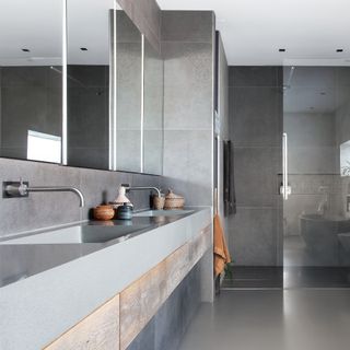 A modern bathroom with rectangular mirrors on wall with LED lighting, grey large wall tiles and shower enclosure with glass door