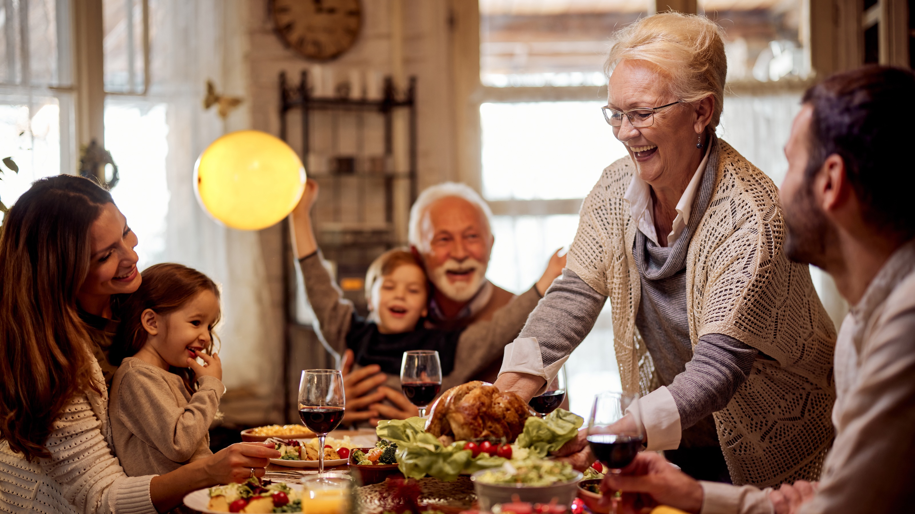 An older woman carves a turkey for a multigenerational family dinner.