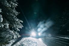 Light from the headlights of a car on a winter road surrounded by snowy forest at night