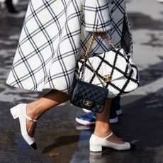 A guest at Paris Fashion Week crossing the road holding a checkered Chanel bag