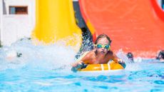 boy in goggles going down a water slide into a pool