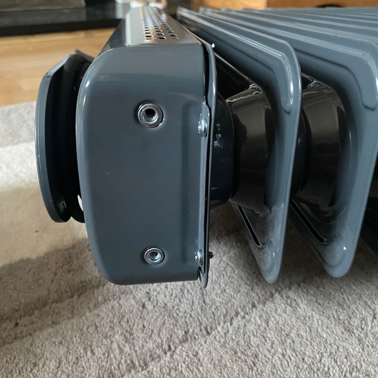 Close up of the wheel holes on the base of the Morphy Richards HeatFlux 2.5kW Digital Oil-filled Radiator, while it's laid flat on a neutral rug