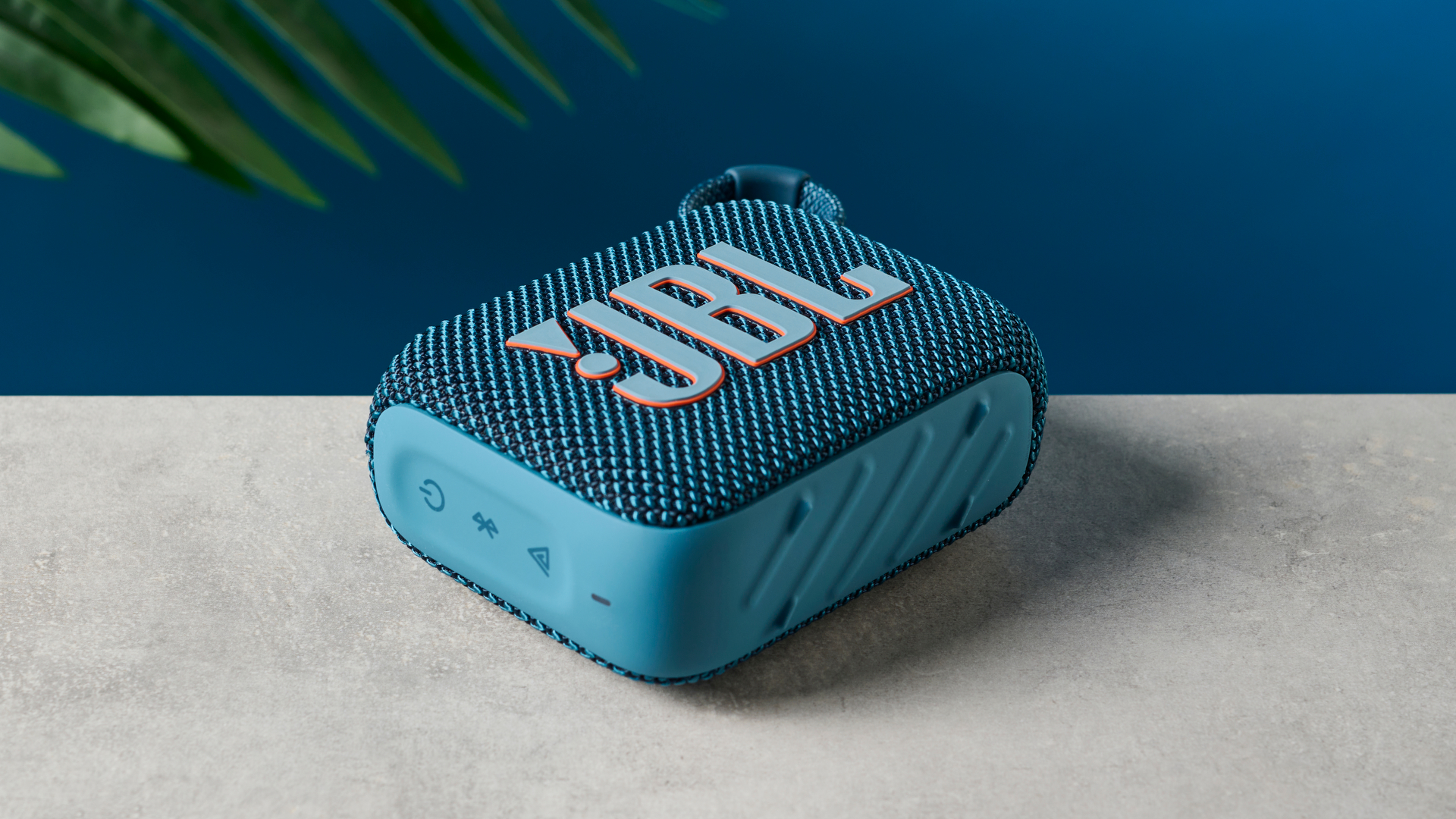 A photo of the JBL Go 4 in blue on a concrete surface against a blue wall.