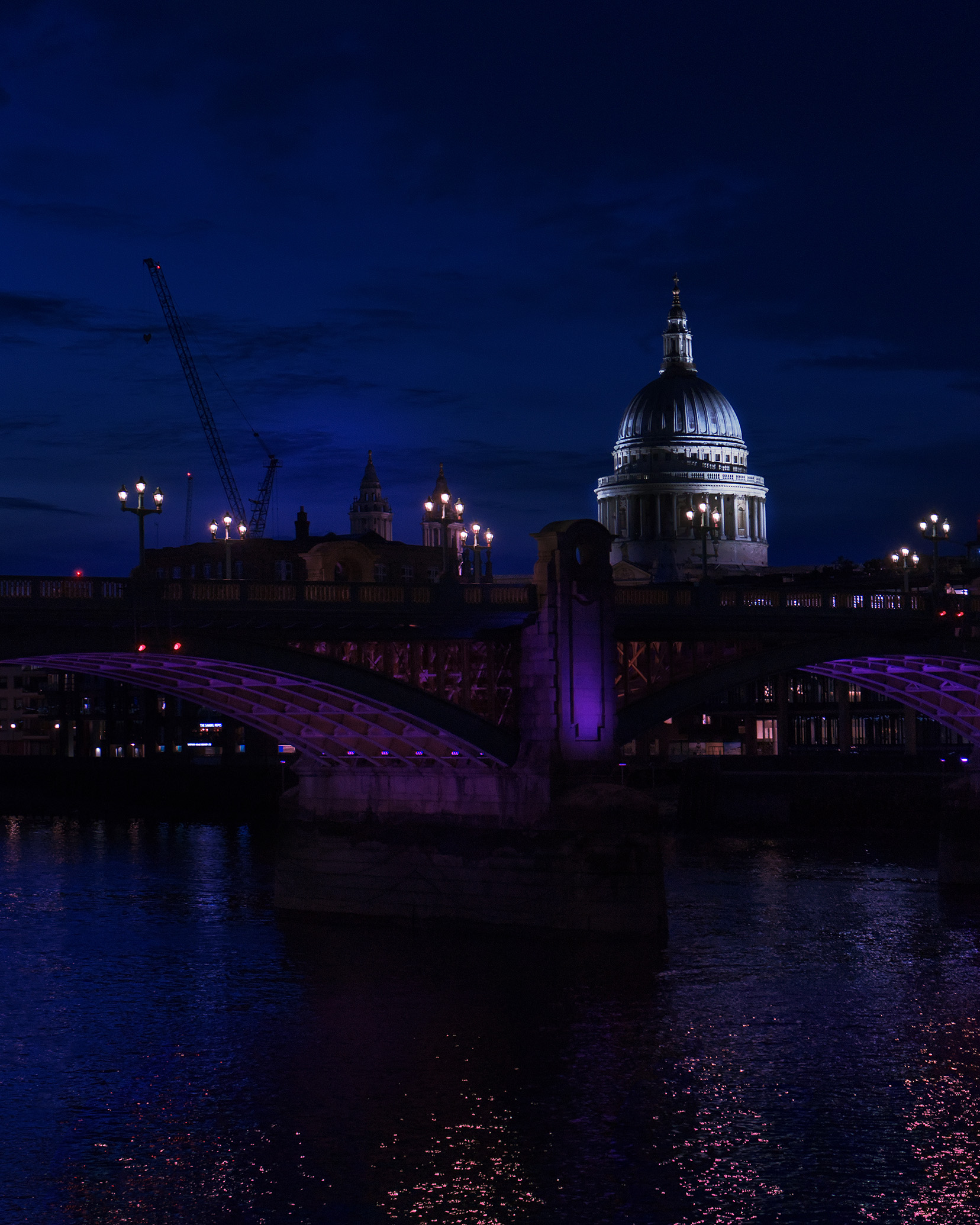 St. Paul's Cathedral illuminated at night, viewed across a softly lit bridge with reflections shimmering on the water below